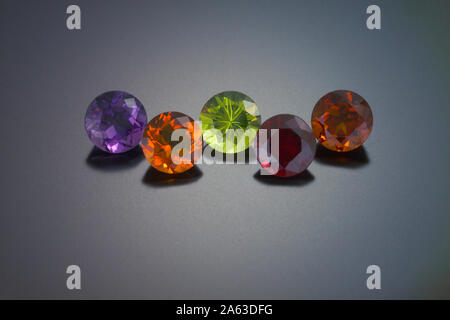 A round cut amethyst, citrine, peridot, red garnet and a fire citrine are shown on a grey reflective background. Stock Photo