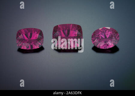 Three red-purple faceted garnet gemstones sit on a black reflective background. There is one oval and two pincushion rectangle stones. Stock Photo