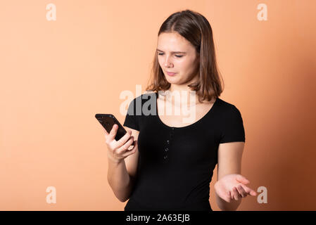Girl shows discontent with a smartphone, on a light orange background. Stock Photo