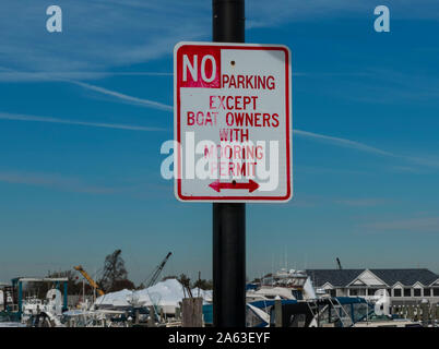 A sign on a lamp post in a marina reads No Parking except boat owners with mooring permit. Stock Photo