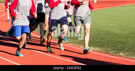 Group of high school boys running fast on a red track while wearing spikes Stock Photo