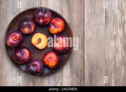 Ripe purple plum fruits on the wooden  background. One plum in cut and other are whole. Fruity still life. Healthy food. Flat lay with copy space. Stock Photo