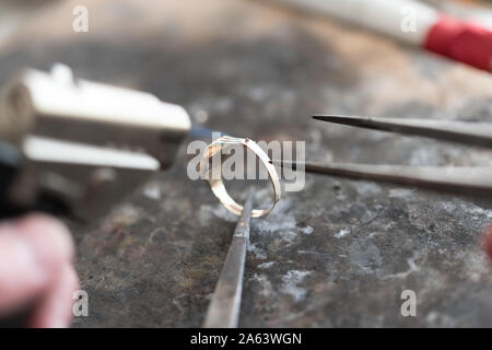 Goldsmith working and soldering an unfinished jewelry piece with a torch  flame at a workbench in workshop Stock Photo - Alamy