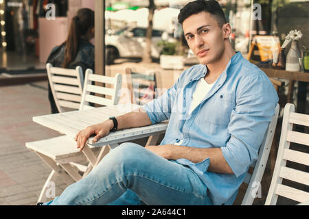 Outdoors Leisure. Stylish guy sitting at cafe on the street looking aside pensive Stock Photo