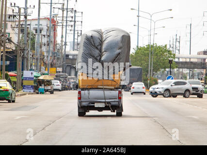 Pickup carries a many paper box on heap covered with large canvas. Car transports pile of goods on street city, Samut Prakan, Thaoland. Stock Photo