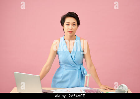 Young beautiful Asian successful businesswoman standing, hands on working desk, smile at camera Stock Photo