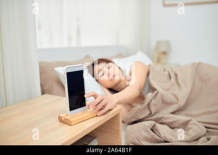 Annoying alarm. Woman lying in bed being woken by mobile phone, turning off noisy signal, closeup Stock Photo