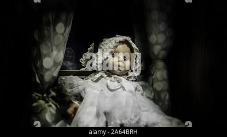 horror vintage baby girl doll with scar face sit against the window, black vignette border effect for Halloween background Stock Photo