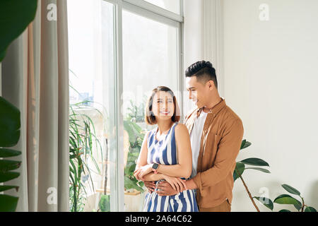 Happy young Asian couple looking through window at home Stock Photo