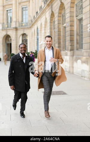 Caucasian european man running with afroamerican male person and holding hands in city. Stock Photo