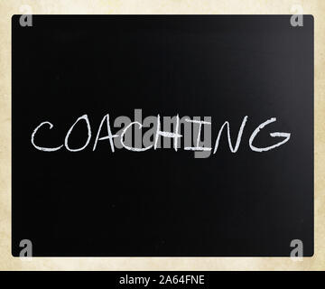 'Coaching' handwritten with white chalk on a blackboard. Stock Photo