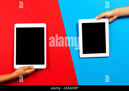 Kids hands holding tablet computer over red and light blue background Stock Photo