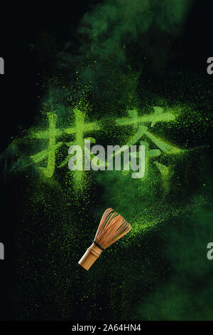 Kanji Matcha written in matcha powder with a bamboo whisk flying in the air. Japanese drink concept on a dark background with copy space Stock Photo