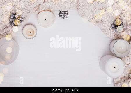 White candles, knitted sweater and pine cones on white background, top view. Stock Photo
