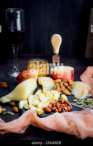 glass of red wine, different varieties of cheese, almond, honey in jar on dark wooden table Stock Photo