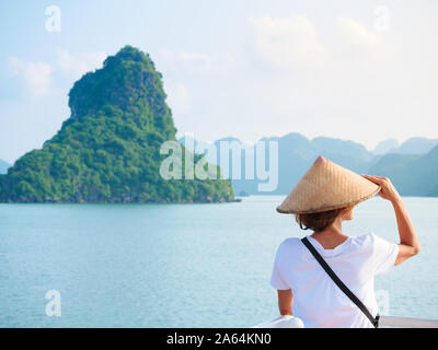 Woman with traditional looking at unique view of Halong Bay, Vietnam. Tourist traveling on cruise among Ha Long Bay rock pinnacles in the sea. Caucasi Stock Photo