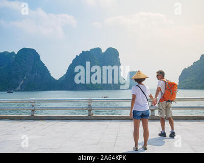 Couple walking hand in hand on promenade at Halong City, Vietnam, view of Ha Long Bay rock pinnacles in the sea. Man and Woman having fun traveling to Stock Photo
