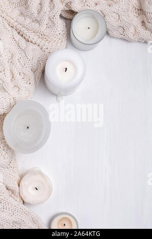 Creative composition with white candles and knitted sweater on the white wooden table Stock Photo