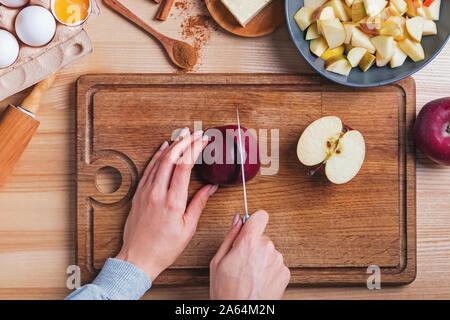 Woman's hands cutting red apple on wooden board, top view. Stock Photo