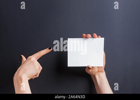 Woman's hands holding blank card with one hand and pointing on it with the finger of another. Stock Photo