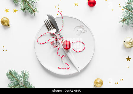 Christmas Table Setting with fir branch and red ornaments on white, flat lay, top view. Christmas dinner, party design, concept - table setting with f Stock Photo