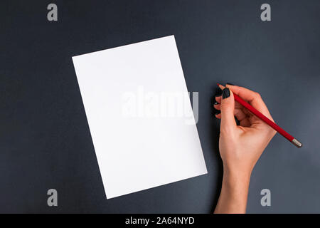 Woman's hand holding red pencil near the blank card on black background Stock Photo