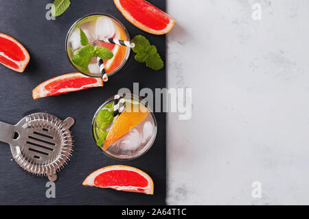 Glasses with drink and pieces of grapefruit on the black slate stone Stock Photo