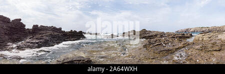 Immersed in the wilderness between rocks sculpted by wind and agitated blu sea with a surreal atmosphere in this huge panoramic 180 degrees view Stock Photo