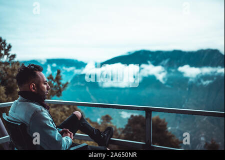 Caucasian Armenian traveler wake up in the mountain cottage with a perfect view on the sunrise over the mountains. Foggy and cool morning. Man drinks Stock Photo