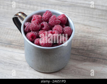 Ripe sweet raspberries in old rustic metal cup on wooden background. Stock Photo