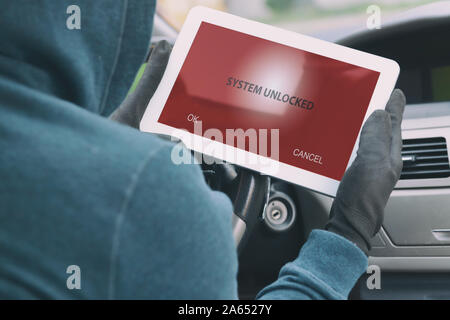 Hooded thief tries to break the car's security systems with tablet. Hacking modern car concept Stock Photo