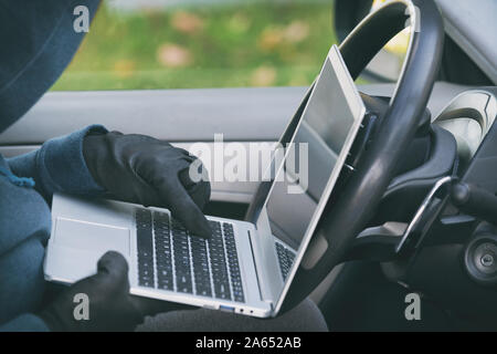 Hooded thief tries to break the car's security systems with laptop. Hacking modern car concept Stock Photo