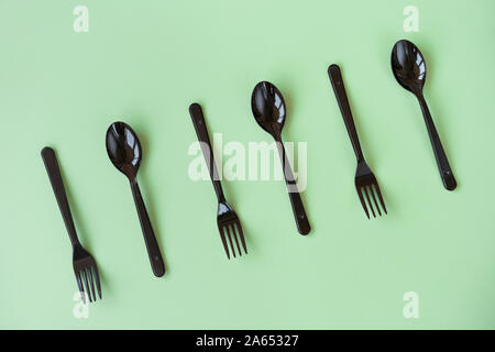 Black plastic spoons and forks lay on a green background in neo light Stock Photo