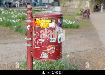 MUENSTER, GERMANY - MARCH 30, 2019: A garbage bin full of waste and covered with stickers and messages stands in a park in Muenster, Germany on March Stock Photo