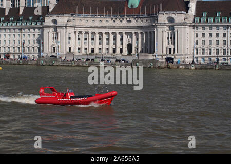 A red speed boat traveling upstream on the River Thames at Westminster Bridge, London, with City Hall in the background and sightseers Stock Photo