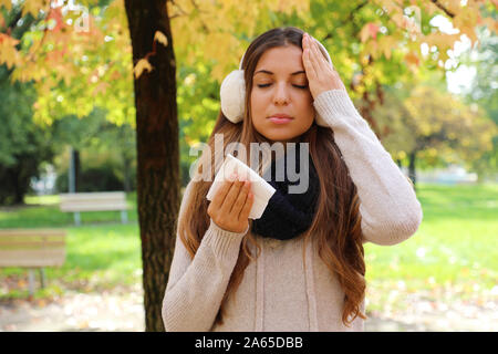 Young woman suffering headache cold fever holding paper tissue outdoors. Stock Photo