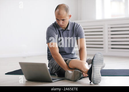 Young disabled man sitting on the floor and watching sports lesson on laptop computer in the room Stock Photo