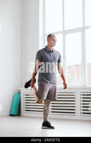 Young disabled man standing and stretching his leg during relaxation exercise in gym Stock Photo