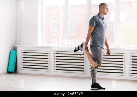 Young disabled man with prosthesis leg standing and doing exercises in the gym Stock Photo