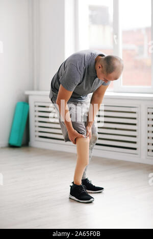 Young man standing in the room and touching his prosthesis leg Stock Photo