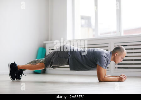 Young disabled man in sports clothing doing push-ups during sports training in the gym Stock Photo