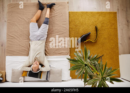 High angle view of young disabled man relaxing on the bed and enjoying the music in his wireless headphones in the room Stock Photo