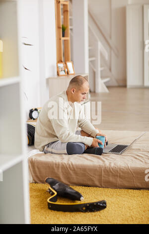 Young man sitting on the bed and using laptop computer in work in the bedroom Stock Photo