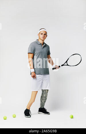 Portrait of young disabled sportsman in sports clothing holding racket and looking at camera over white background Stock Photo