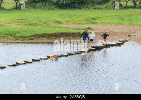 Three people and dog crossing the Ewenny River, using the stepping stones near Merthyr Mawr. Viewed from Ogmore castle, Glamorgan, South Wales, UK Stock Photo