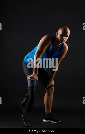 Portrait of young paralympic sportsman with leg prosthesis looking at camera isolated on black background Stock Photo