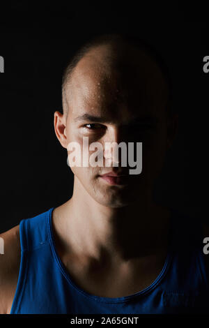 Portrait of serious young man in blue shirt looking at camera isolated on black background Stock Photo