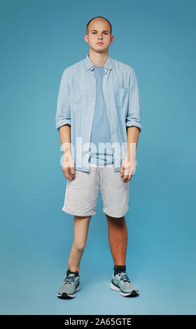 Portrait of young teenager with leg prosthesis in casual clothing standing over blue background Stock Photo