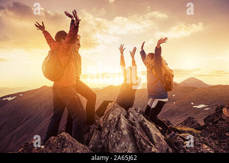 Four happy hikers celebrating climbing on mountain top at sunset Stock Photo