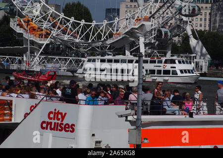 A view of the London Eye from the opposite side of the River Thames with a citycruises passenger boat in the foreground with many people on board Stock Photo